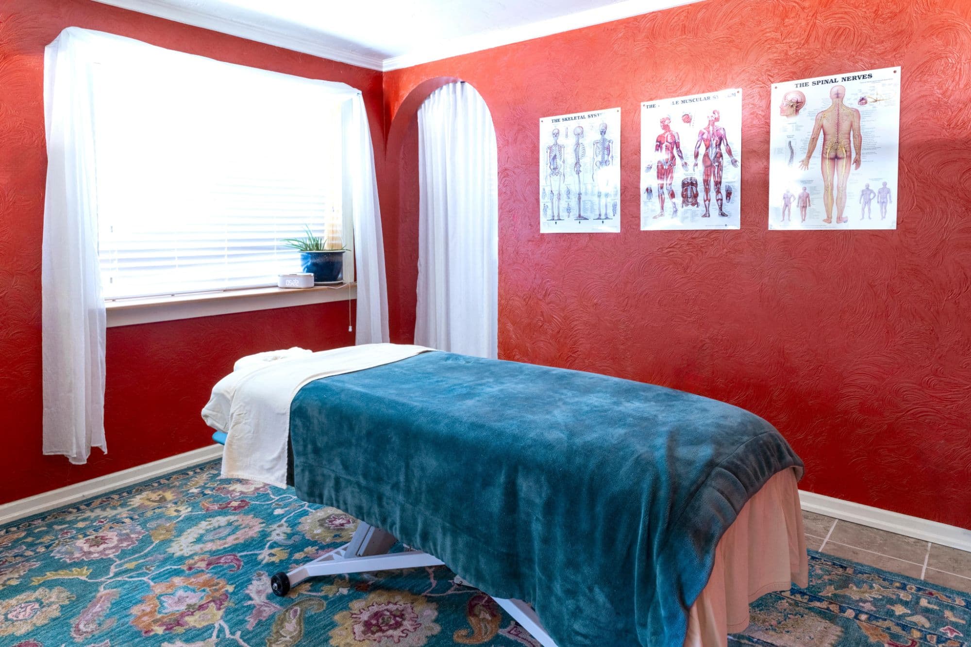 The treatment room at Body Harmony Massage, with a draped massage table, anatomy charts and a patterned rug